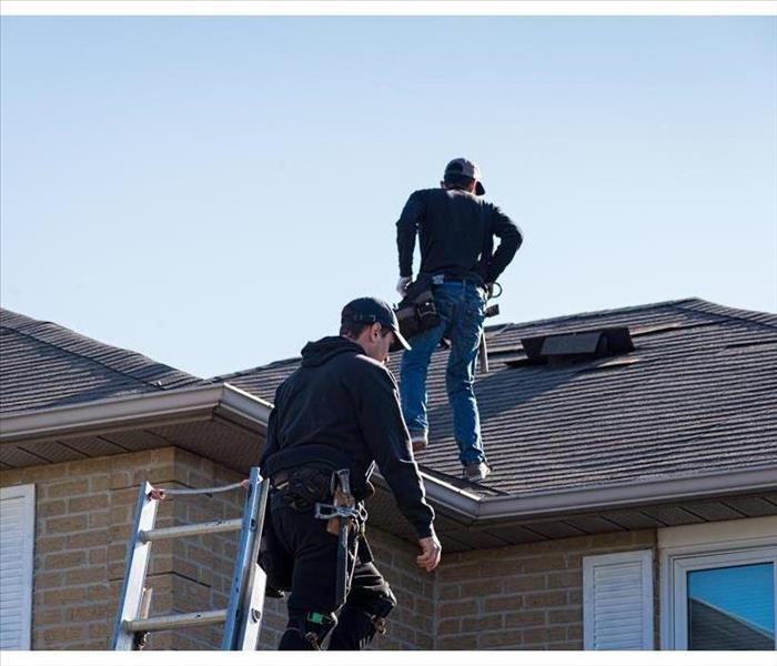 Two men on top of the roof of a house, carrying out inspection